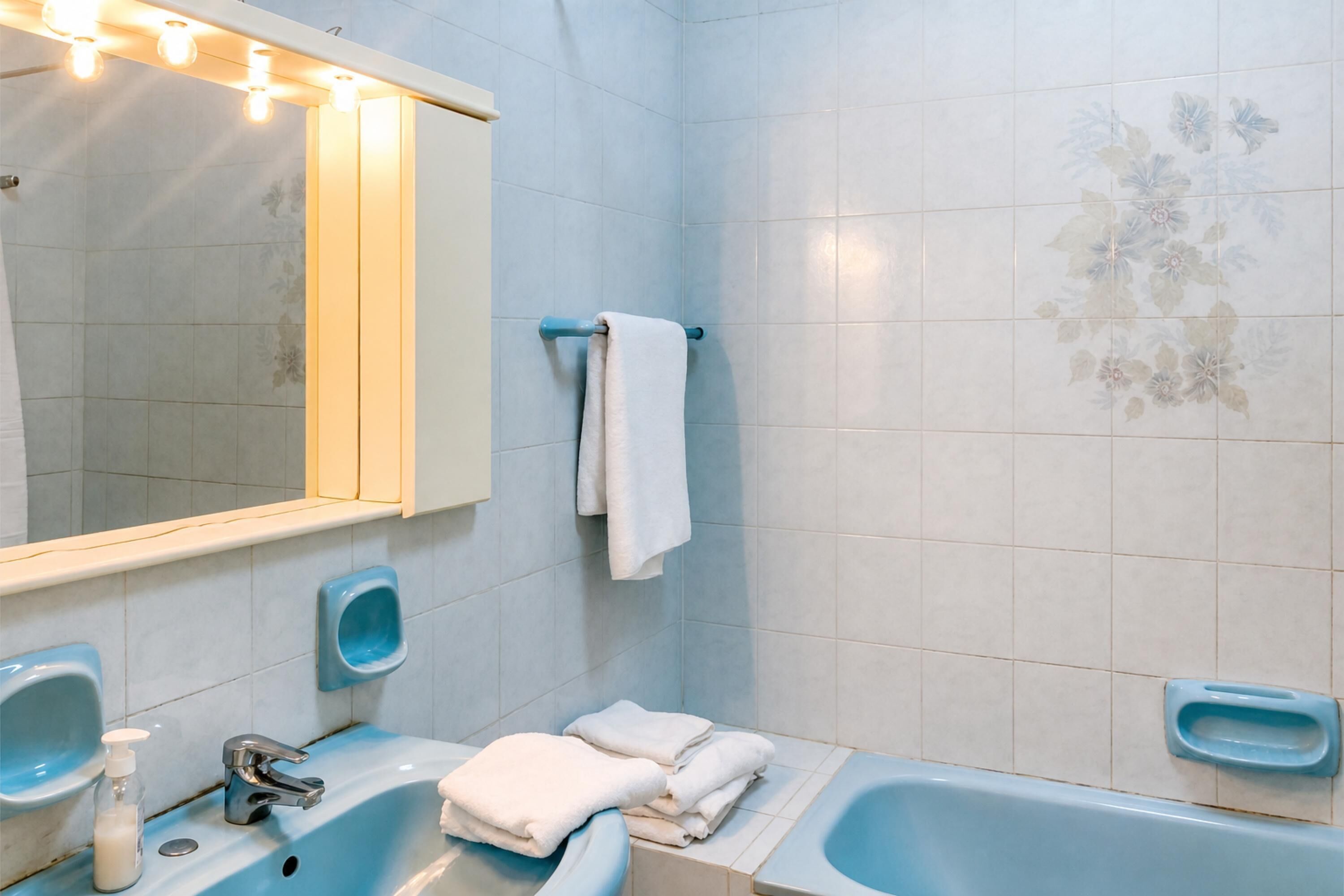 Un baño con un lavabo azul, un espejo, un perchero para toallas y una bañera.