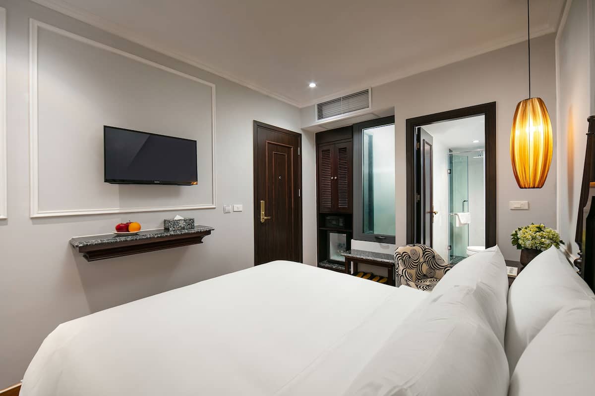 Une chambre d’hôtel avec un grand lit, un téléviseur à écran plat fixé au mur, une petite table avec une chaise et un miroir.