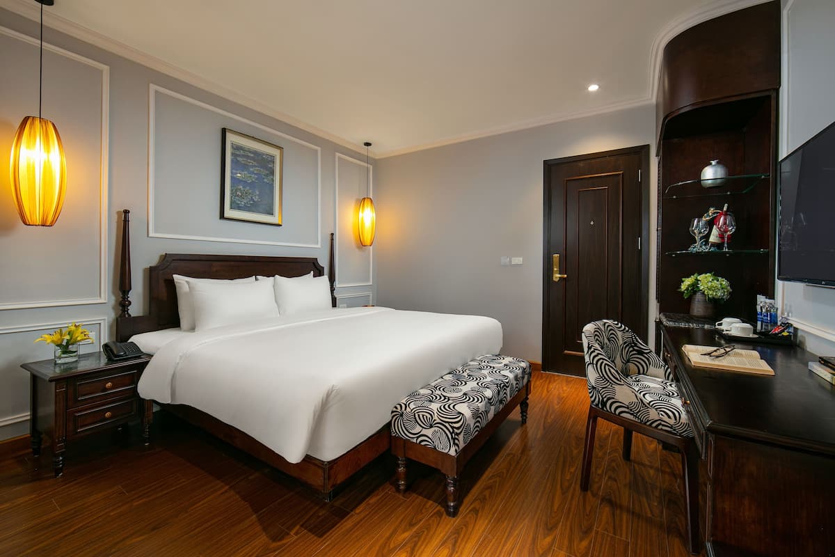 Une chambre d’hôtel bien aménagée, avec un grand lit, des tables de chevet, un bureau avec une chaise et une bibliothèque.