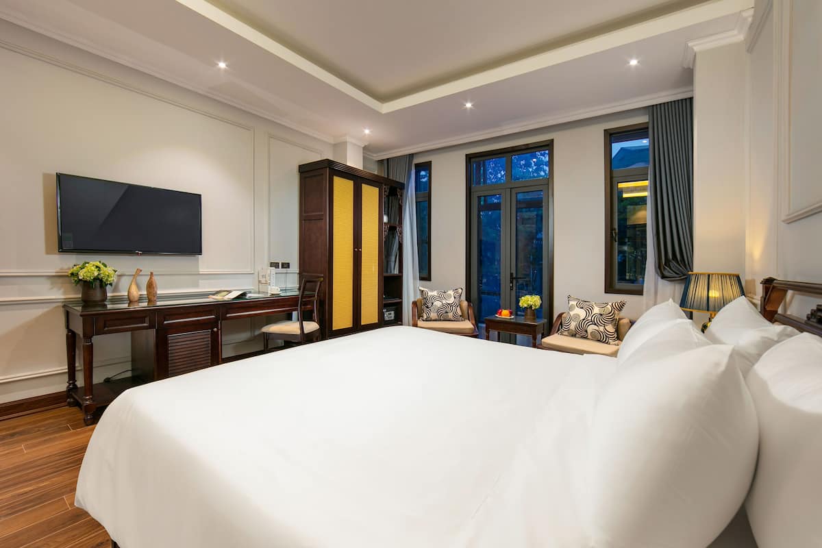 Une chambre d’hôtel avec un grand lit, un bureau, une télévision et une vue sur l’extérieur par les fenêtres.