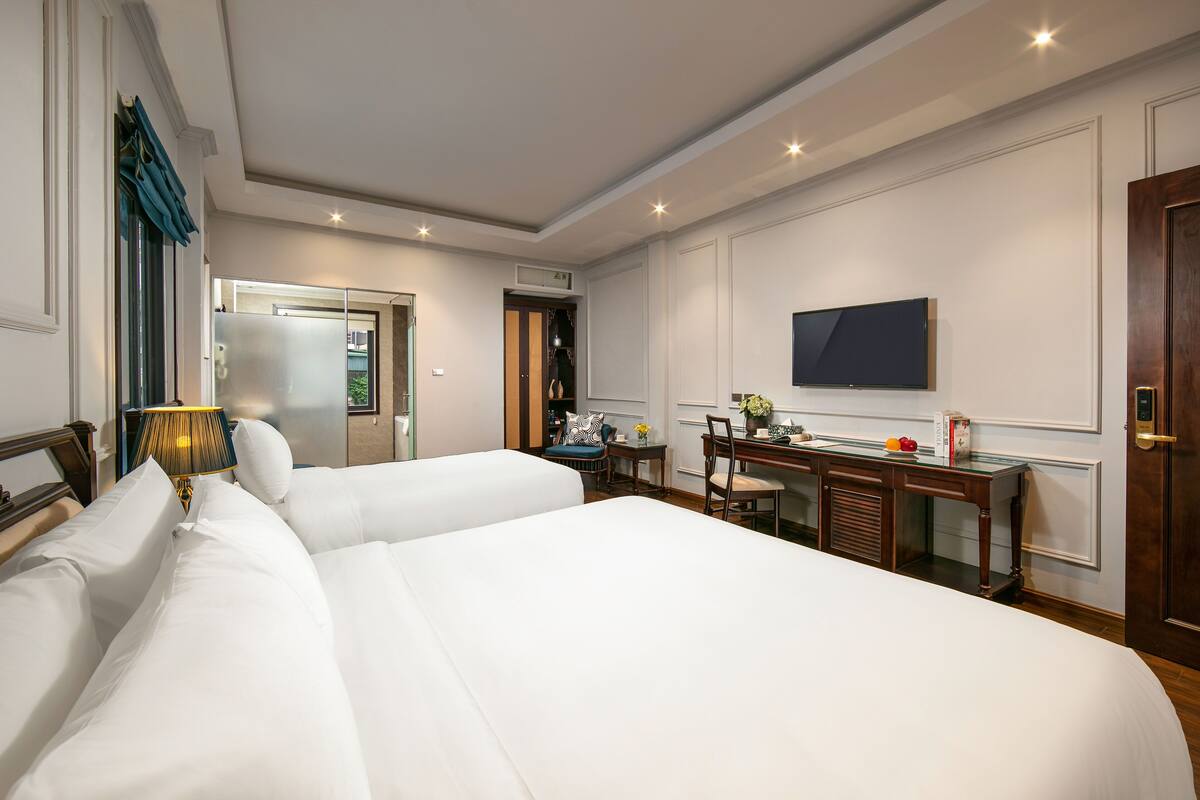 Une chambre d’hôtel avec deux lits, un bureau, une chaise, une télévision et une porte.