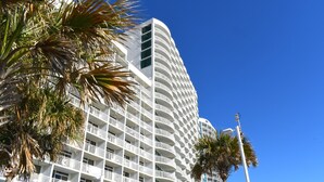 Ein mehrstöckiges Hotel mit geschwungener Fassade, Balkonen und Palmen im Vordergrund.