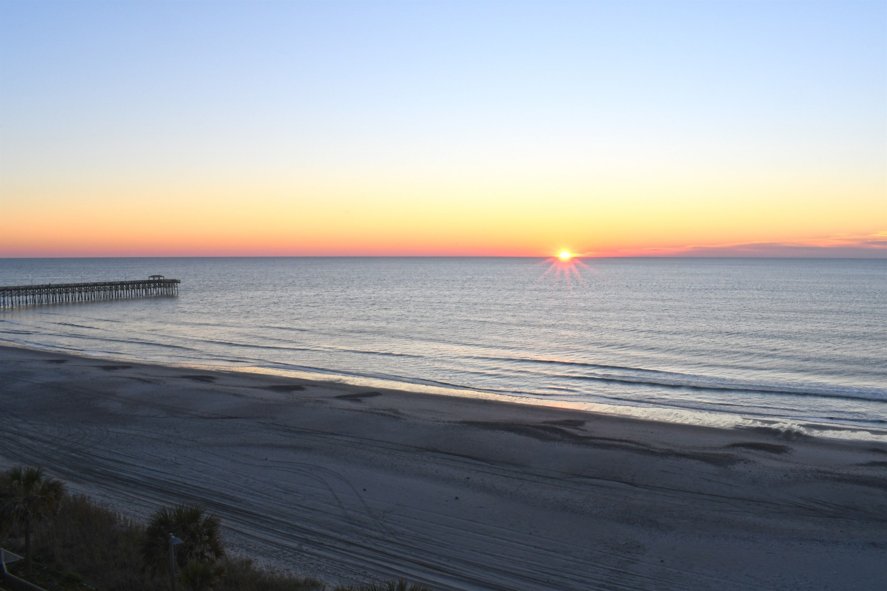 A beach with a pier extending into calm waters during sunset.