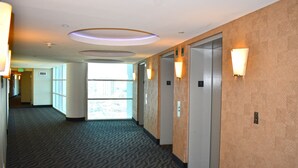 Ein Hotelgang mit Teppichböden, Wandleuchten und einem Aufzug.