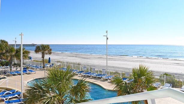 Ein Poolbereich mit Liegestühlen und Blick auf Strand und Meer.