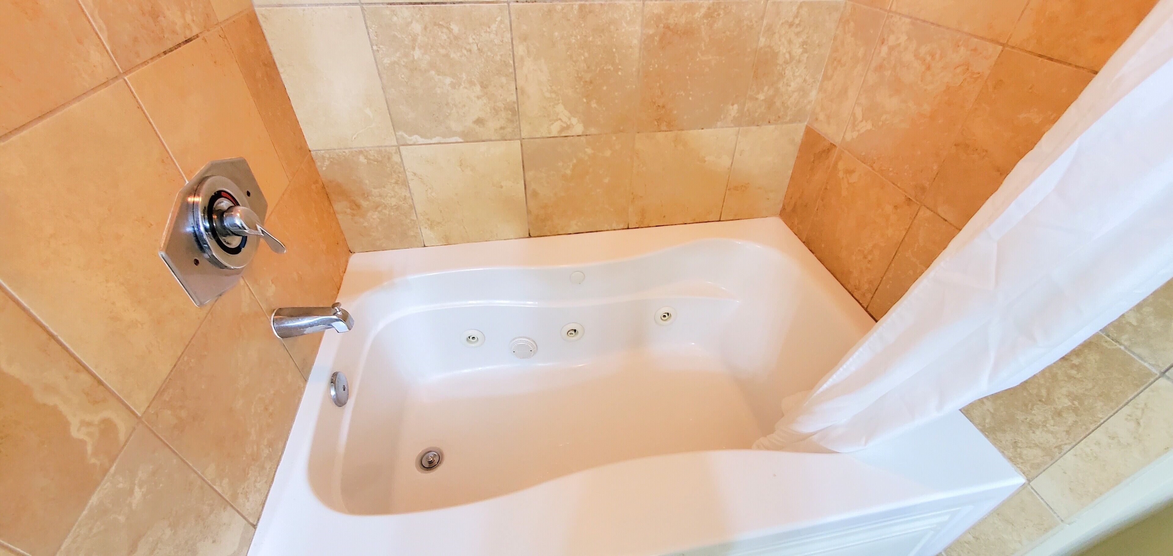 A white bathtub with a shower curtain, a faucet, and a drain.