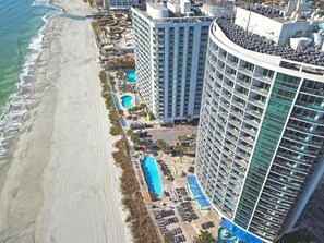 Un hotel de gran altura con varios balcones, una zona de piscina y ubicación frente a la playa.