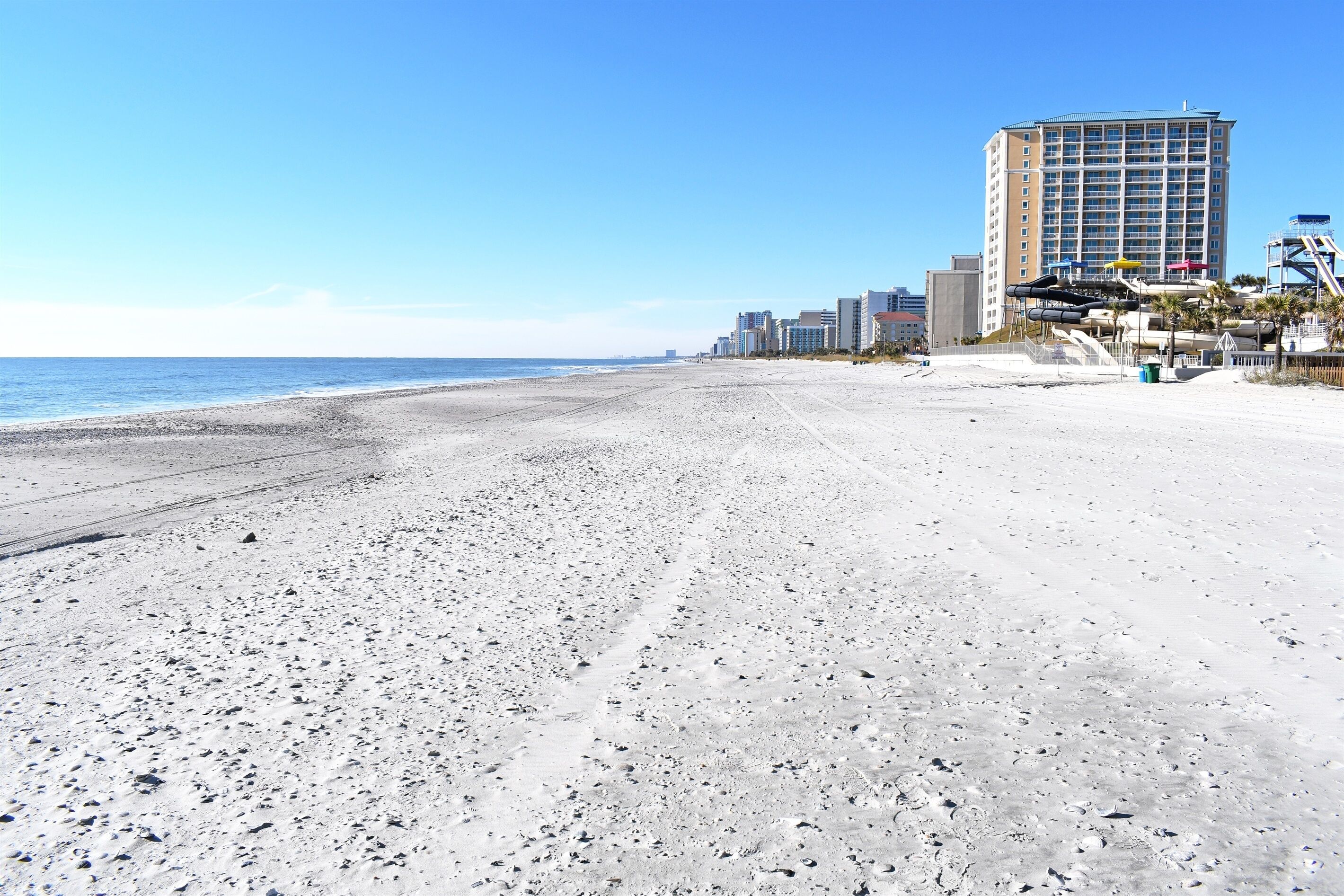 Ein Strand mit einem großen Gebäude im Hintergrund, wolkenlosem Himmel und ruhiger See.