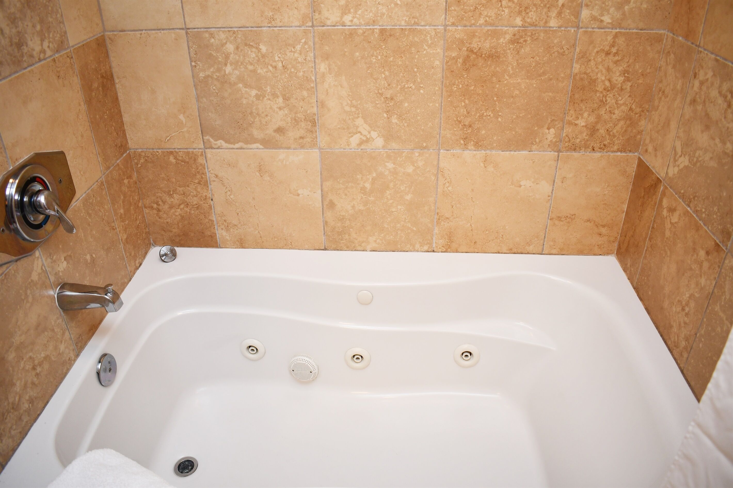 A white bathtub with a handheld showerhead and multiple drain holes.