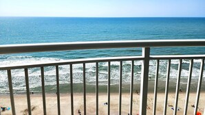 Blick auf einen Strand vom Balkon mit Geländer, Meereswellen und Personen im Sand.