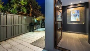 A modern building entrance with a glass door, a tiled pathway, and a fenced area with trees. - Wow Large 4 Bedrooms 4 bathroom with Private pool, 4 min walk to beach (Surfers Paradise)