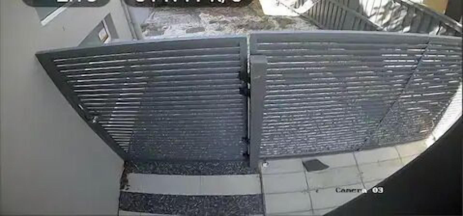 Een beveiligingscamera toont het uiterior van een gebouw, inclusief een groot, donker gebouw met horizontale lijnen.