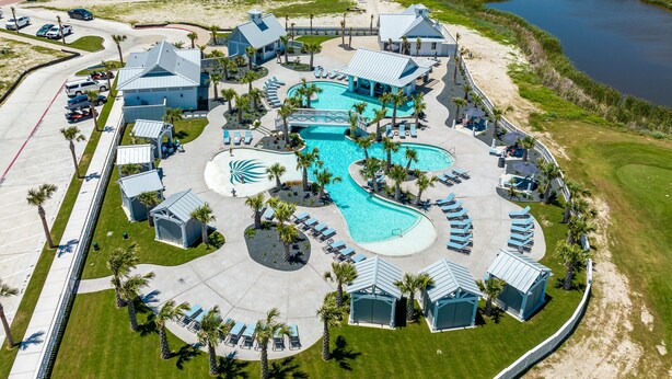 An aerial view of a resort with a large swimming pool, multiple lounge areas, and a parking lot. - Inviting beach-front townhouse with pool, balcony, water views, & W/D (Port Aransas)