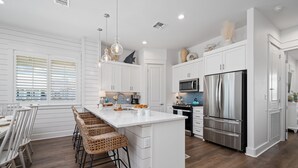A modern kitchen with white cabinetry, stainless steel appliances, and a central island with bar stools. - Inviting beach-front townhouse with pool, balcony, water views, & W/D (Port Aransas)