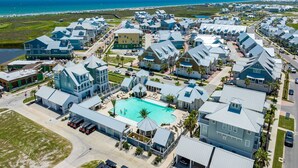 A coastal residential area with multiple houses, a swimming pool, and a beach in the background. - Inviting beach-front townhouse with pool, balcony, water views, & W/D (Port Aransas)