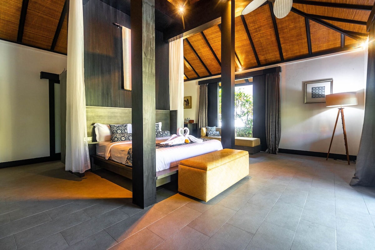 A modern bedroom with a large bed, a bench, and a view of the outdoors.