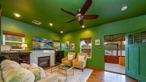 A living room with a fireplace, green walls, a ceiling fan, and a large window.