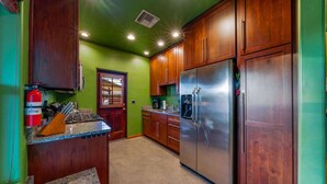A kitchen with wooden cabinets, a stainless steel refrigerator, granite countertops, and a fire extinguisher.