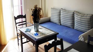 A living room with a sofa, a dining table, chairs, a TV, and a window. - Irigoni Studio - Ikaria (Agios Kirykos)