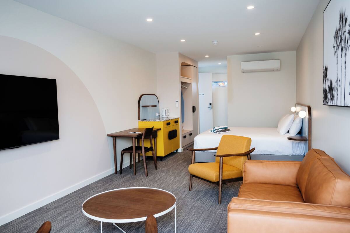 A hotel room with a bed, a desk, a chair, a sofa, and a TV.