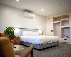 Ein Hotelzimmer mit einem Bett, einem Nachttisch, einem Sessel, einer Pflanze und einem Kleiderschrank.