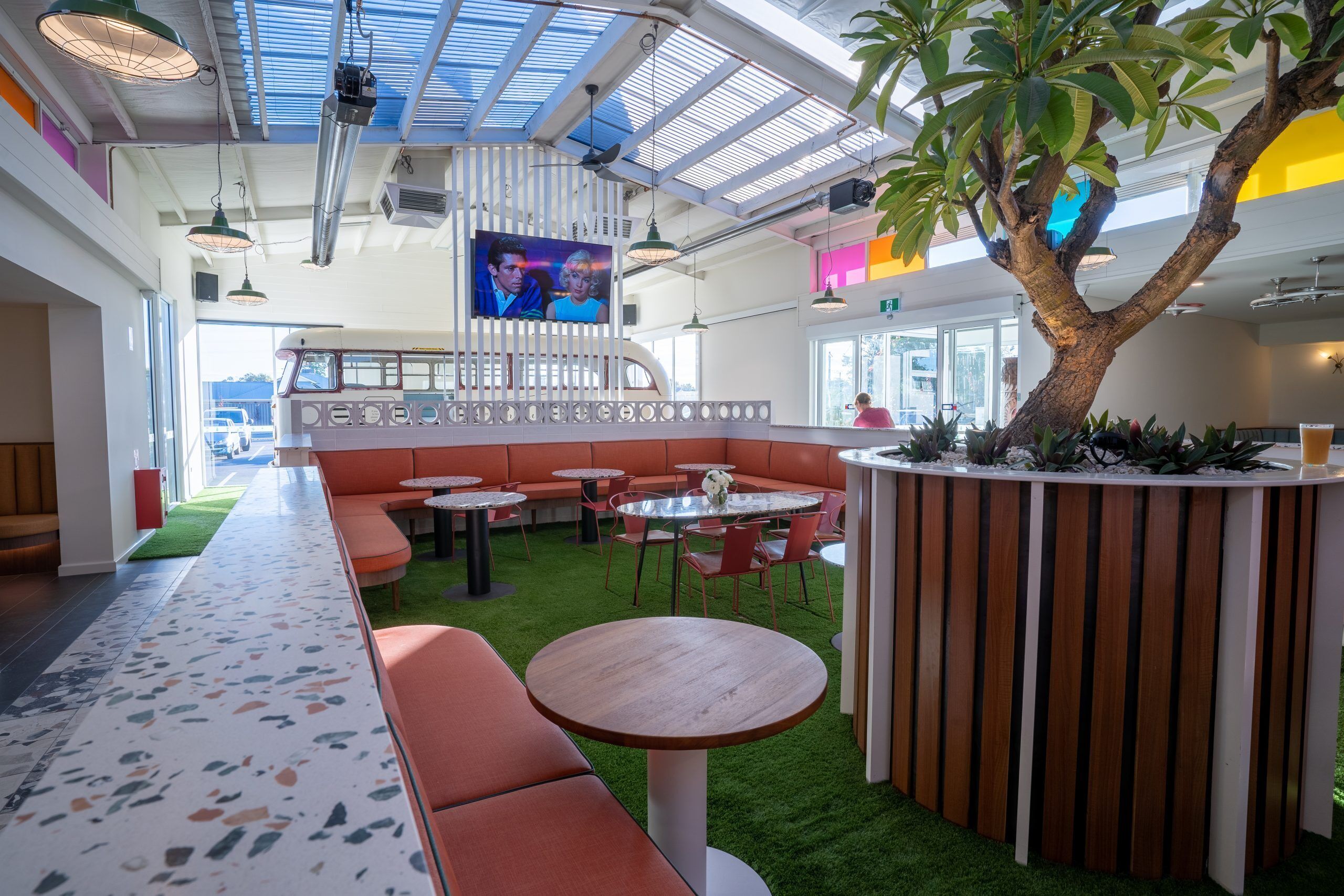 A modern indoor space with seating areas, a central table, and a large tree.