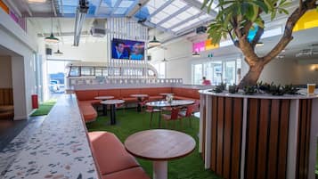 A modern indoor space with seating areas, a central table, and a large tree.
