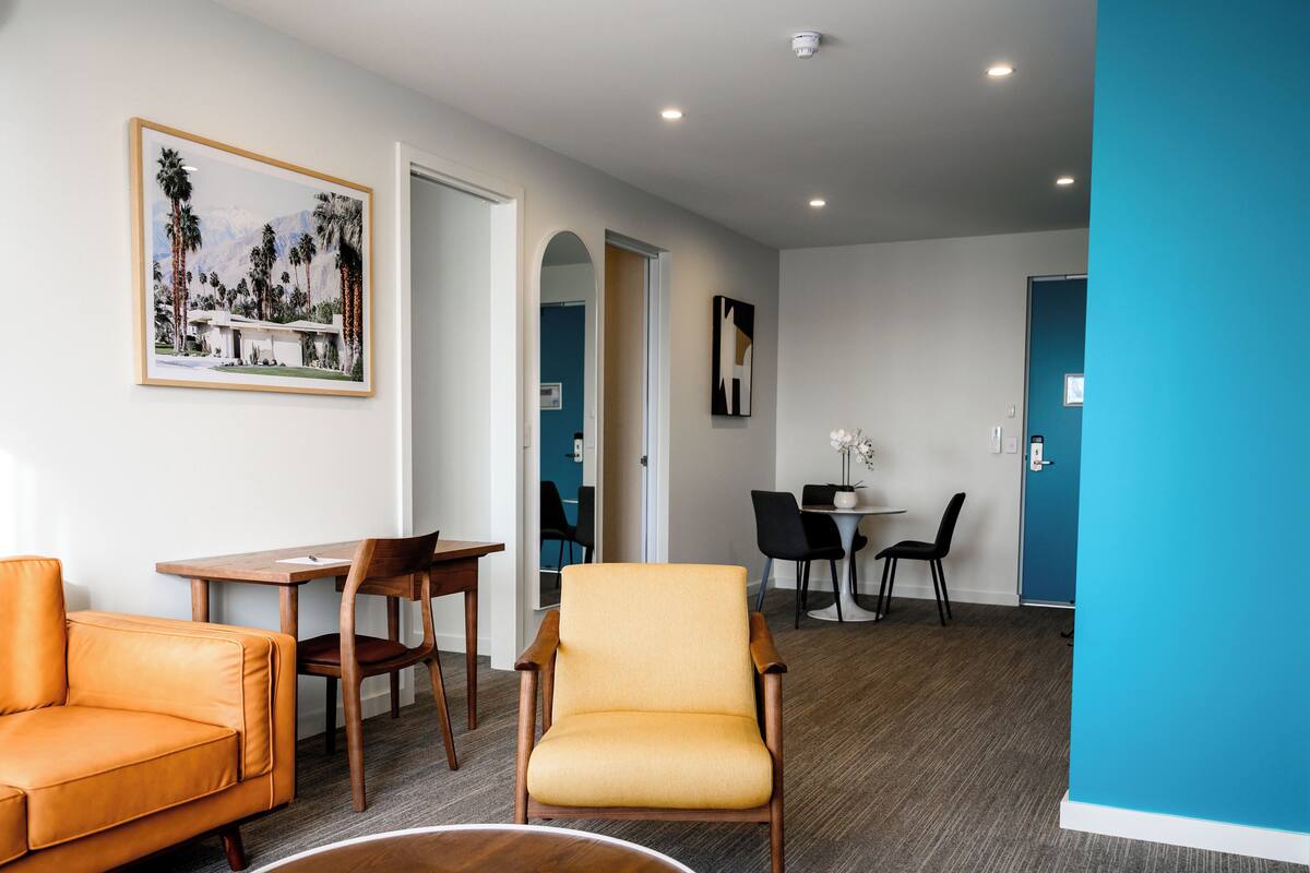 A modern hotel room with a wooden dining table, two chairs, a sofa, and a round coffee table.