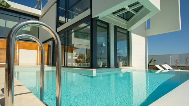 Un edificio moderno con piscina, amplios ventanales de vidrio y una escalera metálica para la piscina.