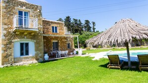 Une maison en pierre dotée d’un balcon, d’une piscine et d’une toiture en chaume.