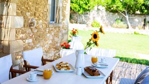 Une façade en pierre, avec une table dressée pour le petit-déjeuner, comprenant des croissants, une miche de pain et une carafe de jus d’orange.