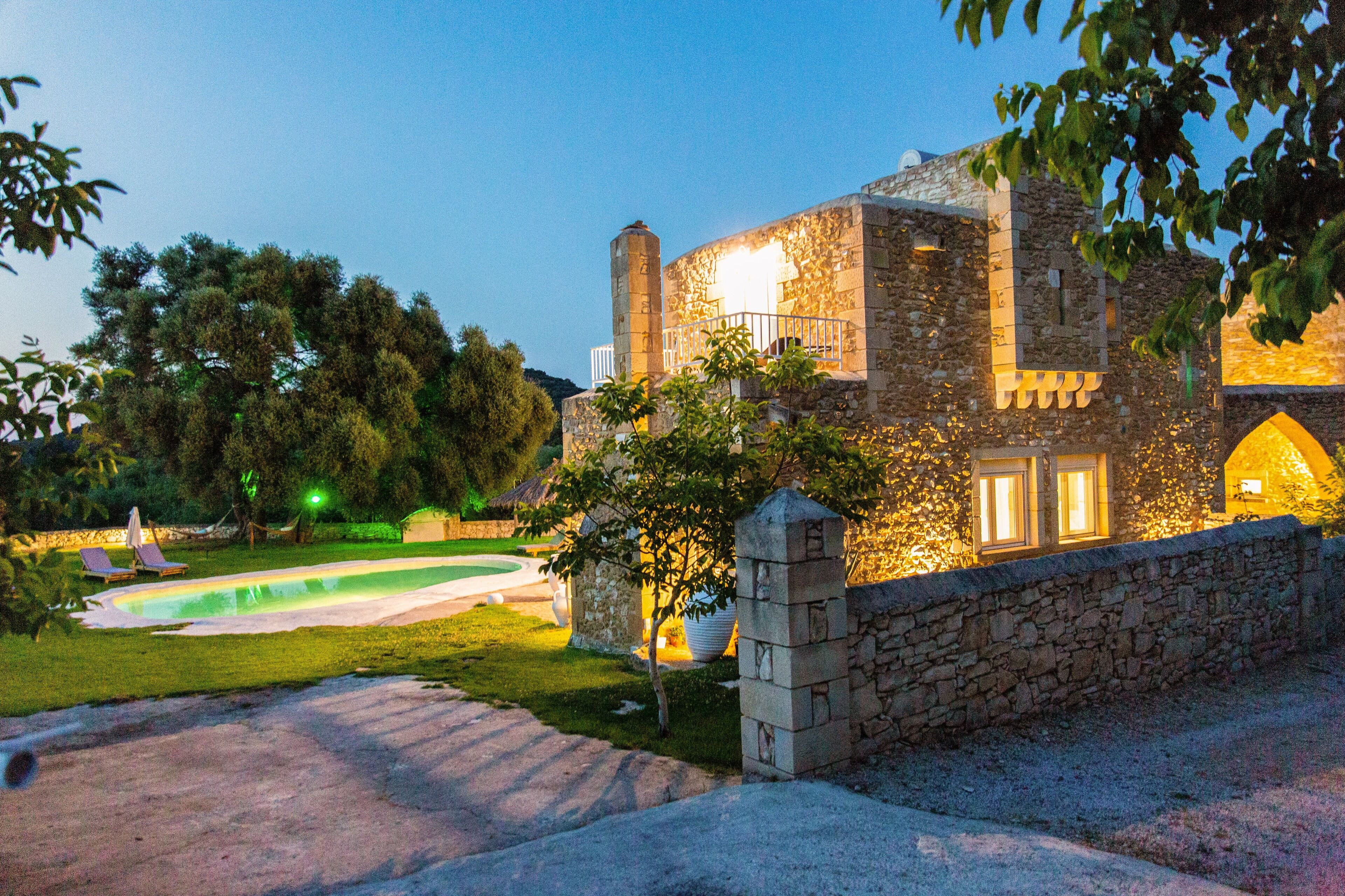 A stone building with a swimming pool, a stone wall, and a small garden.