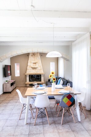 A dining area with a stone fireplace, white chairs, and a table set for four.