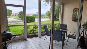 A room with a glass door leading to a patio. The patio has a tiled floor, a table with chairs, and a ceiling fan.