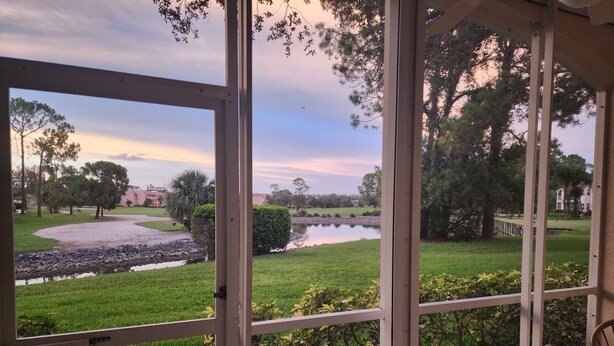 A view from a covered porch with a glass door, overlooking a grassy area with trees and a body of water.