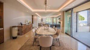 A modern dining area with a marble table and comfortable chairs, a wooden cabinet, and a large window offering a view of the outdoors.