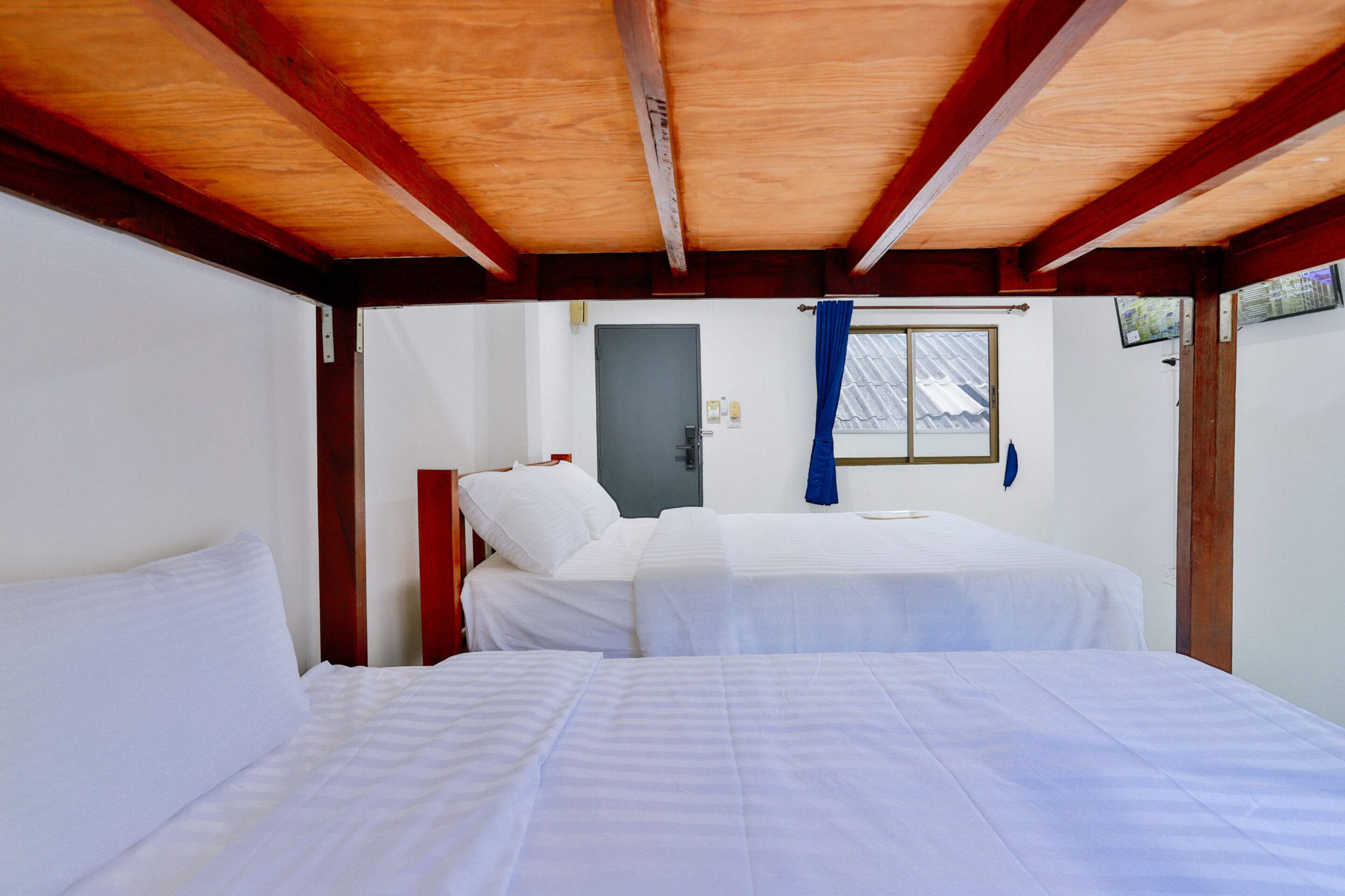 Una habitación con dos camas, vigas de madera en el techo, una ventana con cortina y una puerta.
