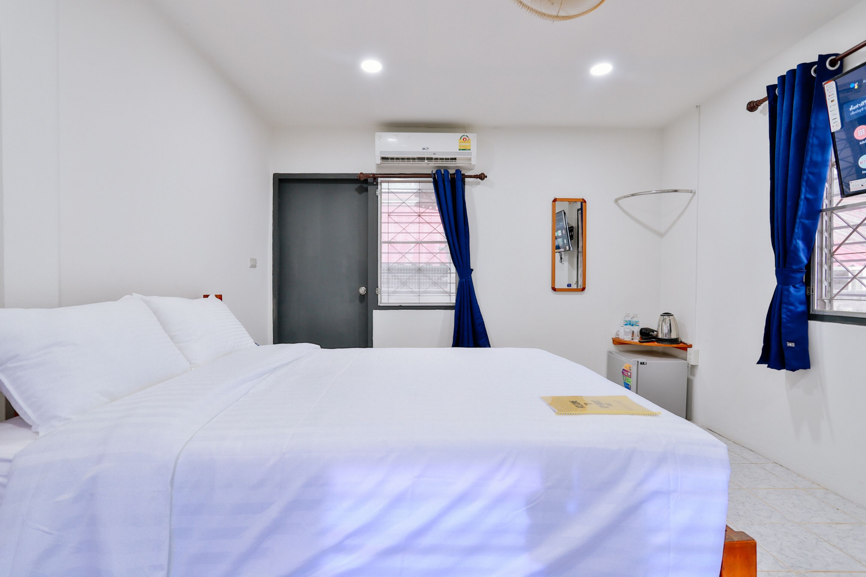 Una habitación de hotel con cama, unidad de aire acondicionado, refrigerador pequeño y ventana con cortinas.