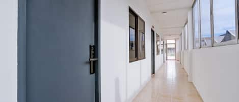 A long, narrow hallway with a blue door on the left, large windows on the right, and a tiled floor.
