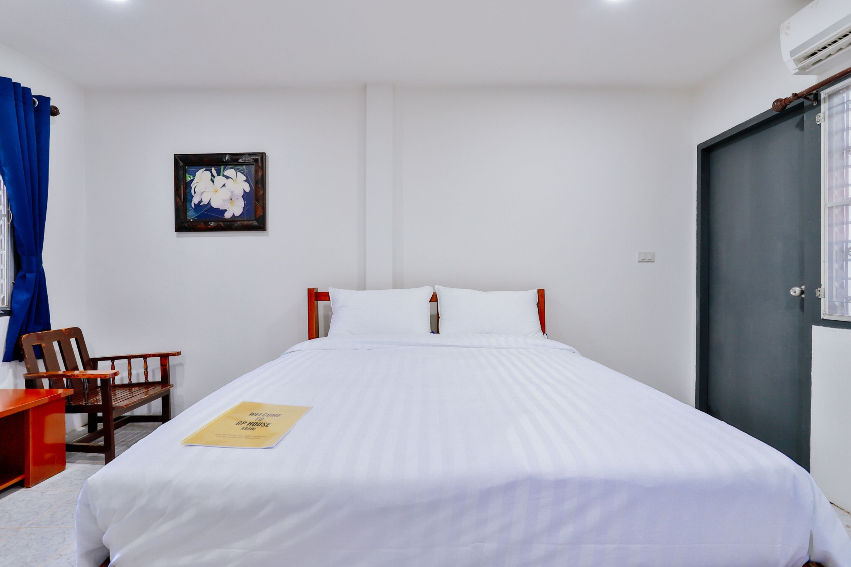 Een hotelkamer met een bed, een houten stoel, een bureau, een lijst met een foto aan de muur en een deur.