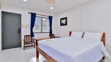A hotel room with a bed, a desk, a chair, a window with curtains, a door, and a ceiling fan.