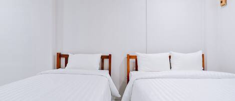 A clean, minimalist room with two single beds, wooden headboards, white bedding, and a small wall-mounted device.