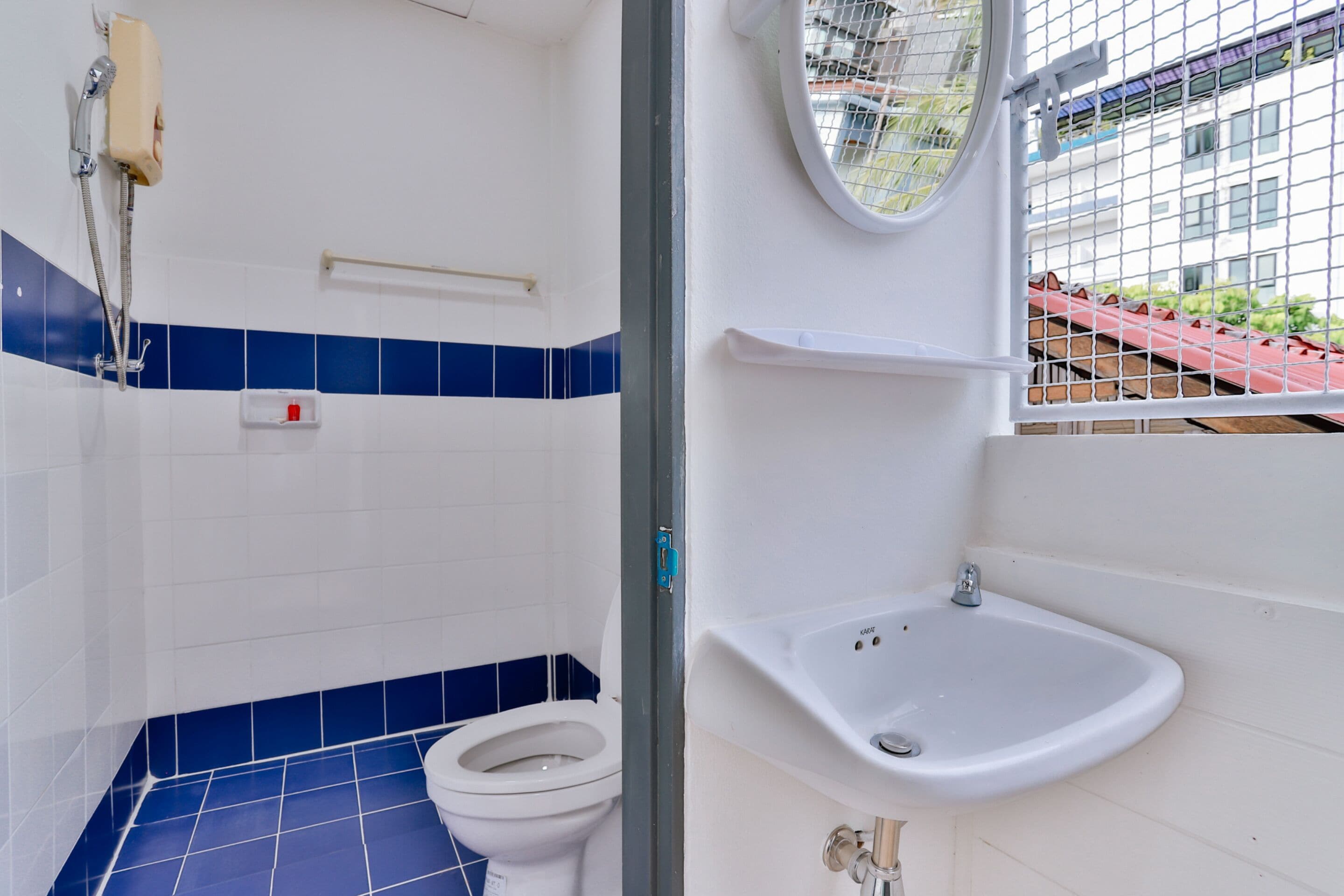 Et badeværelse med toilet, brusebad, vask og et vindue med udsigt til bygninger.