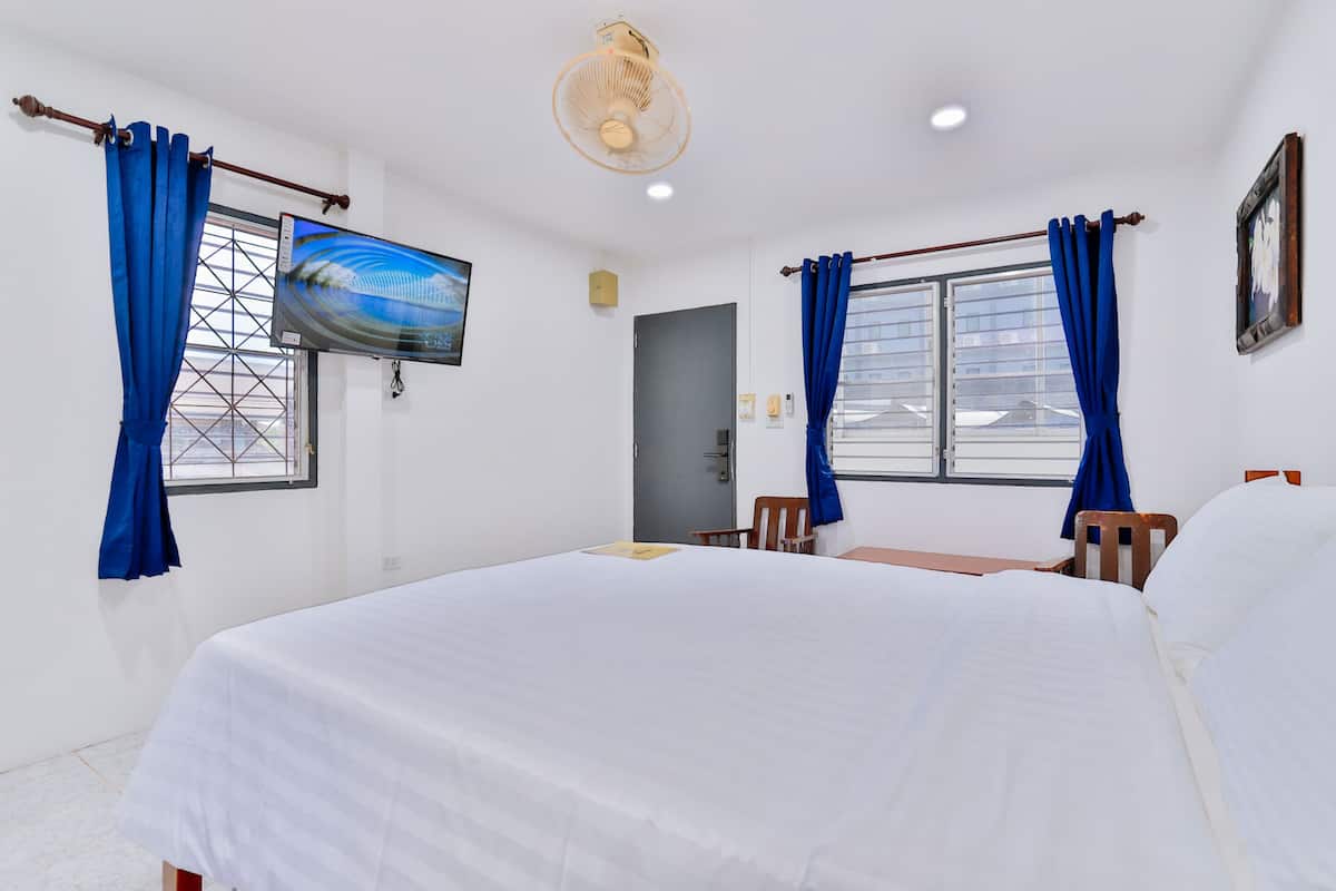 A hotel room with a bed, a television, a fan, and a window with curtains.