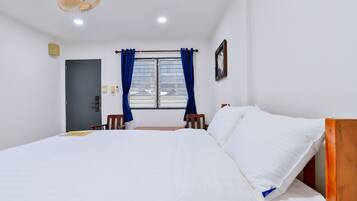 A hotel room with a bed, a window with curtains, a door, and a ceiling fan.