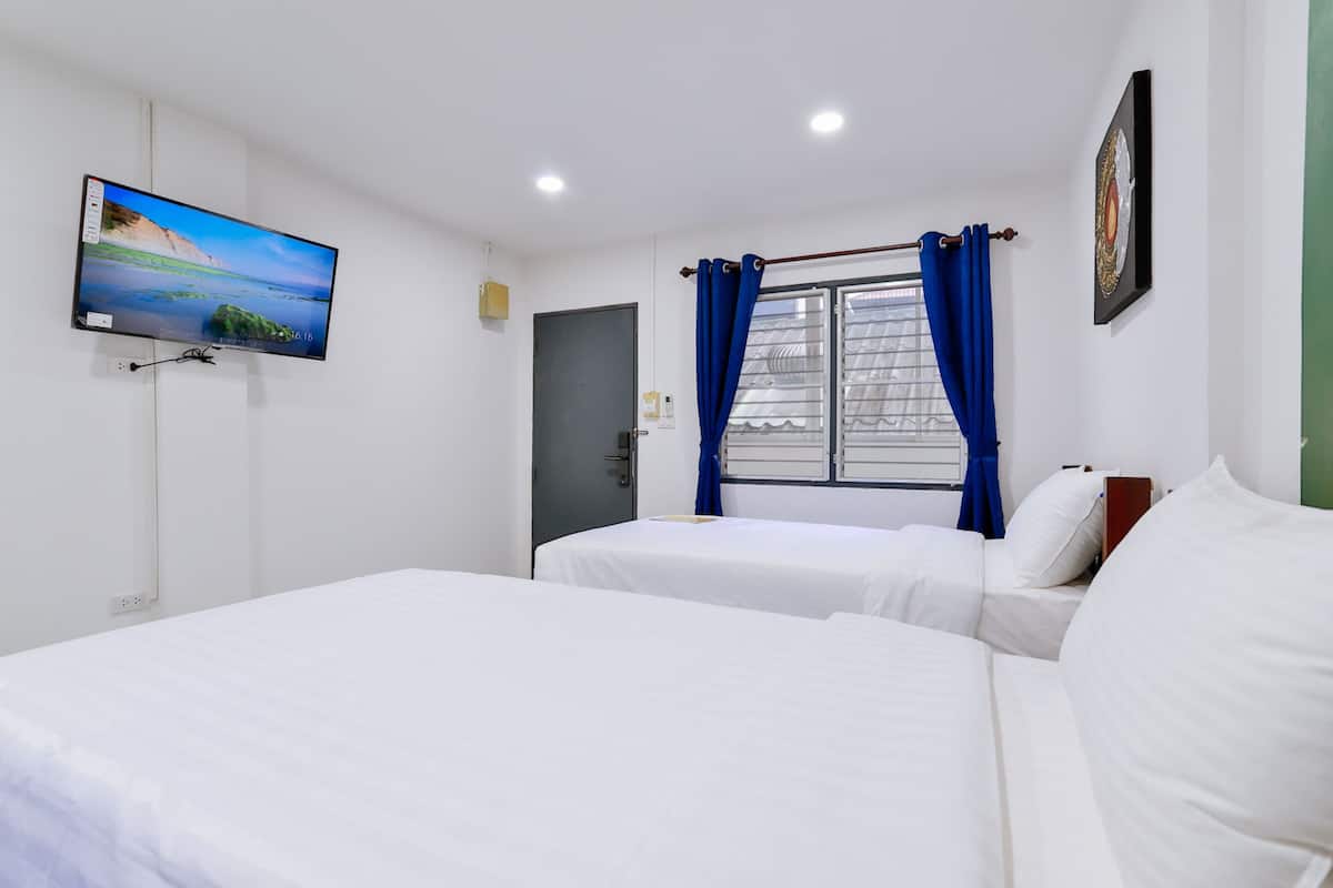 A hotel room with two beds, a TV on the wall, a window with blue curtains, and a door.