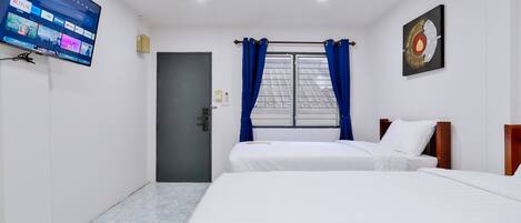 Habitación de hotel con dos camas, un televisor montado en la pared, una ventana con cortinas azules y una puerta.