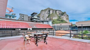 En tagterrasse med et bord og stole, en parabolantenne samt bygninger med rødt tag og en klippe i baggrunden.