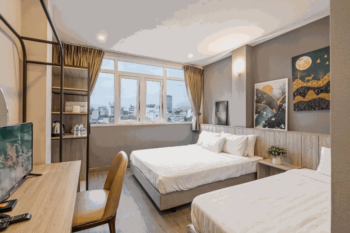Een hotelkamer met twee bedden, een bureau met stoel, een televisie en uitzicht op de stad.