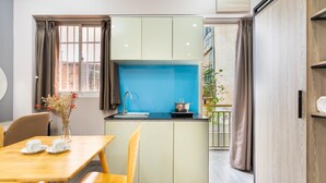 A compact kitchen with a blue backsplash, a dining area with a wooden table and chairs, and a view of the outside balcony. - THE COZY INN (Ho Chi Minh City)